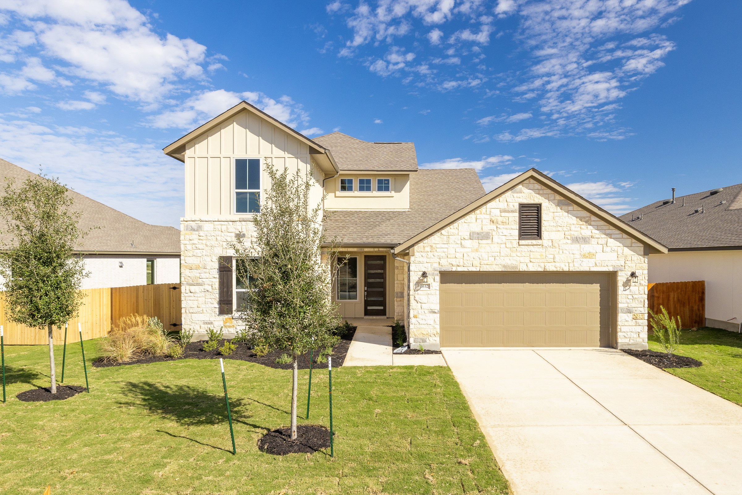 Front view of newly available move-in ready home with spacious lawn, trees in front yard, and tan accent colors
